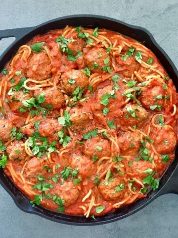 Cast iron skillet full with spaghetti and meatballs with sriracha sauce.