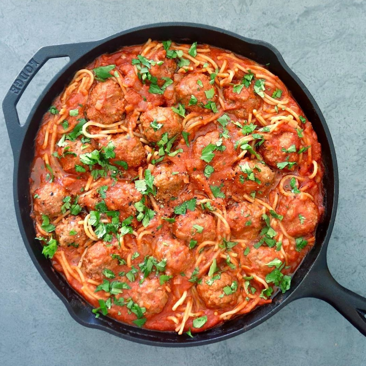Rich-Slow-Cooked-Flavor—No All-Day-Commitment Spicy Sriracha Spaghetti And Meatballs in a cast iron skillet on a gray background.