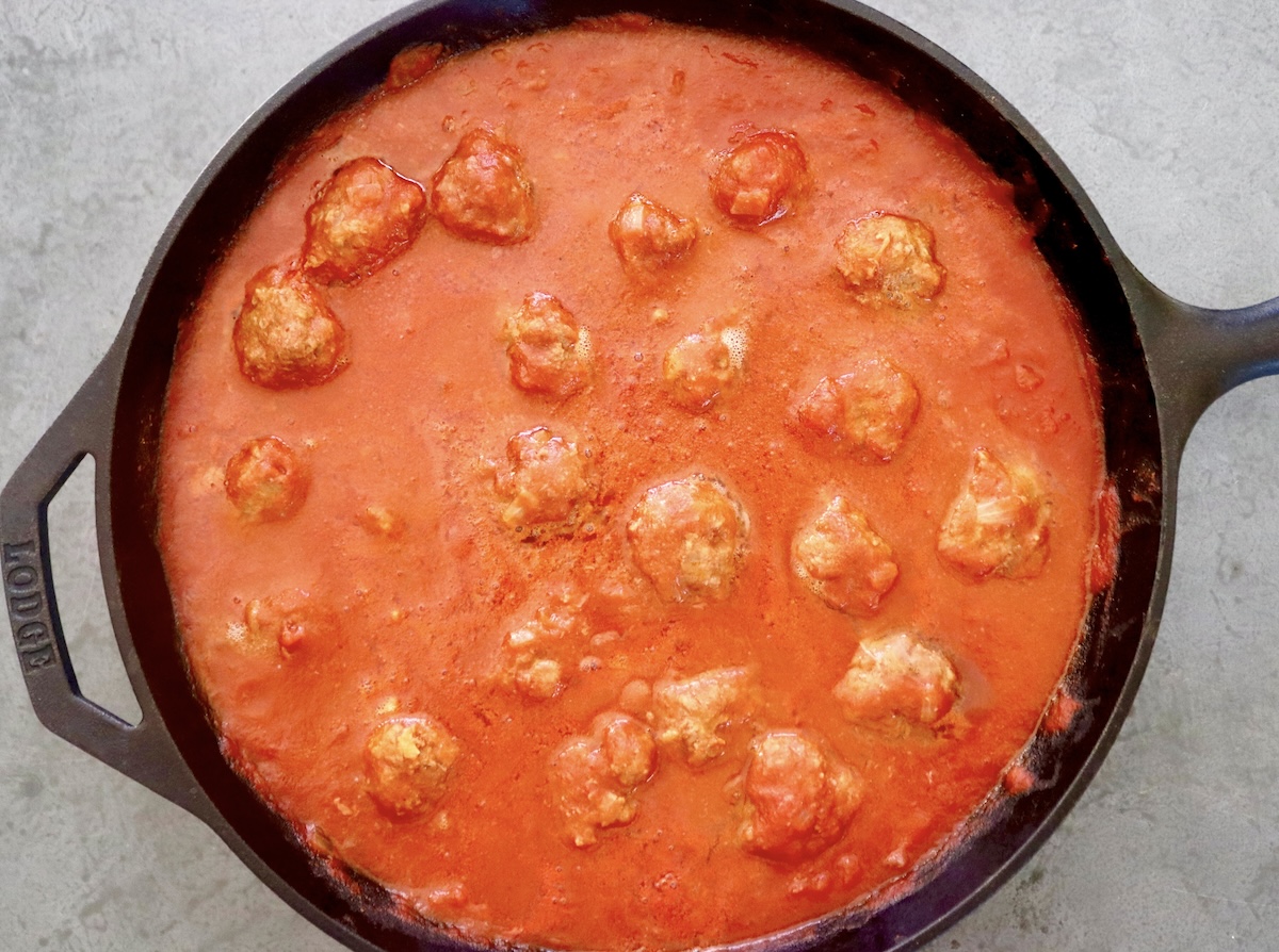 Cast iron skillet filled with tomato sriracha sauce and over a dozen cooked meatballs.