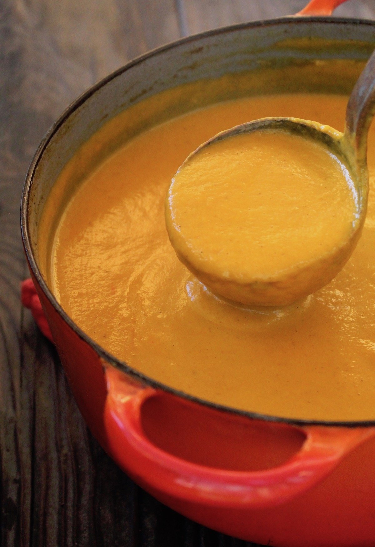 thick coconut carrot soup in a red dutch onve with ladle