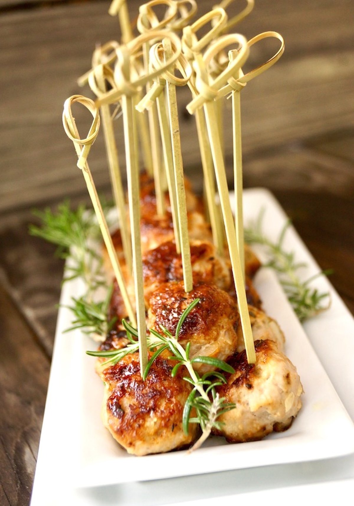 Rosemary-Turkey-Meatballs-with-Honey Rosemary turkey meatballs on white plate with toothpicks.