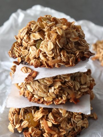 Stack of 3 granola cookies with a square of parchment between each one.