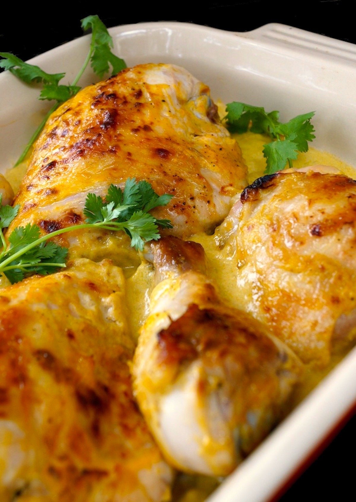 Close up of chicken pieces on the bone baked in mango coconut sauce in a baking dish with fresh cilantro.