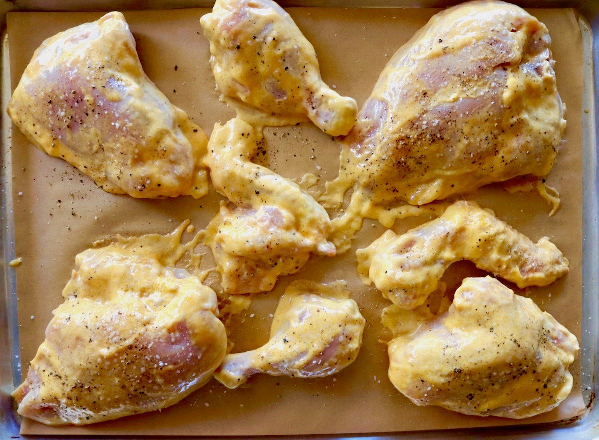 Raw pieces of chicken on the bone with mango marinade on a parchment lined baking sheet.