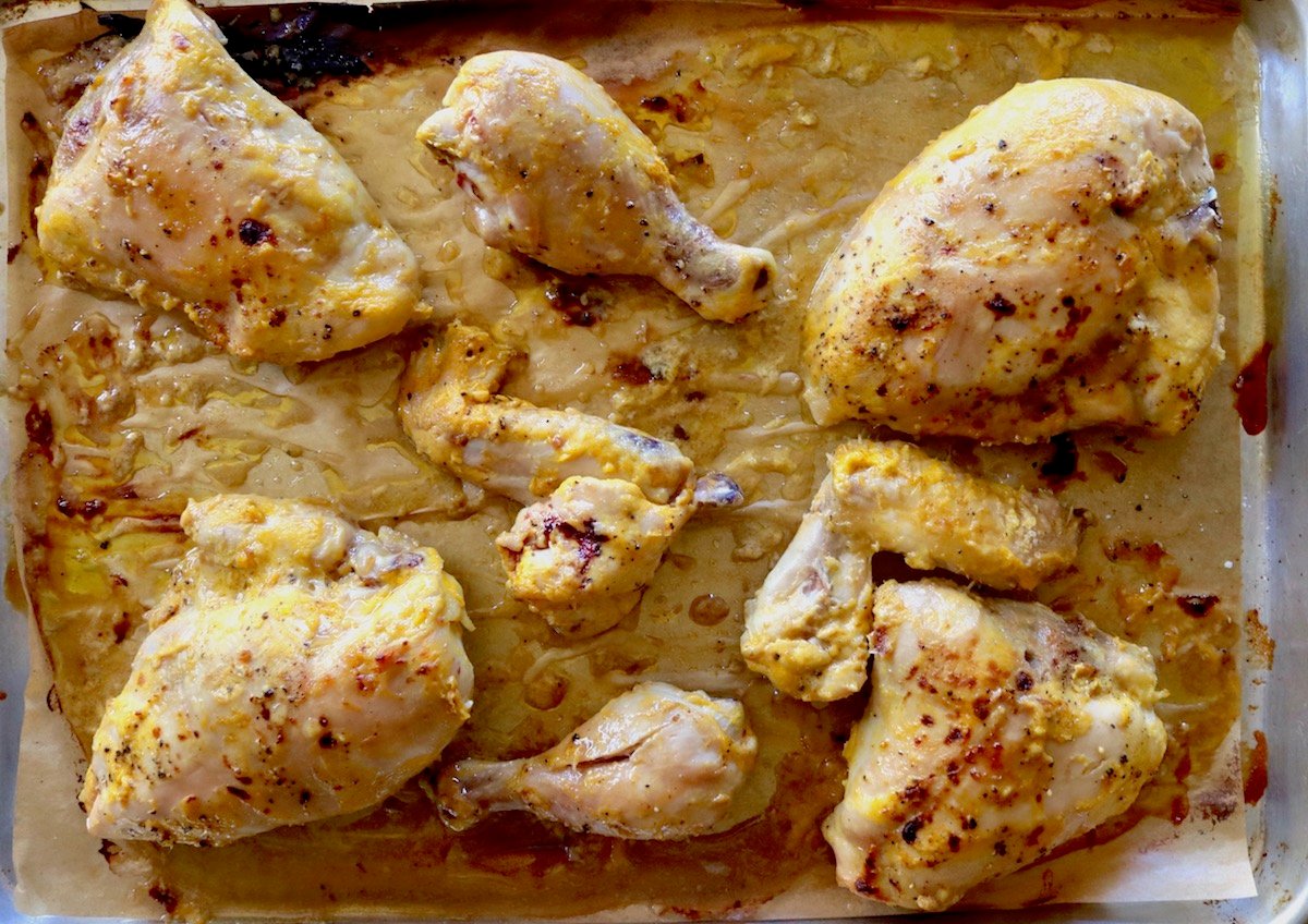 Baked pieces of chicken on the bone with mango marinade on a parchment lined baking sheet.