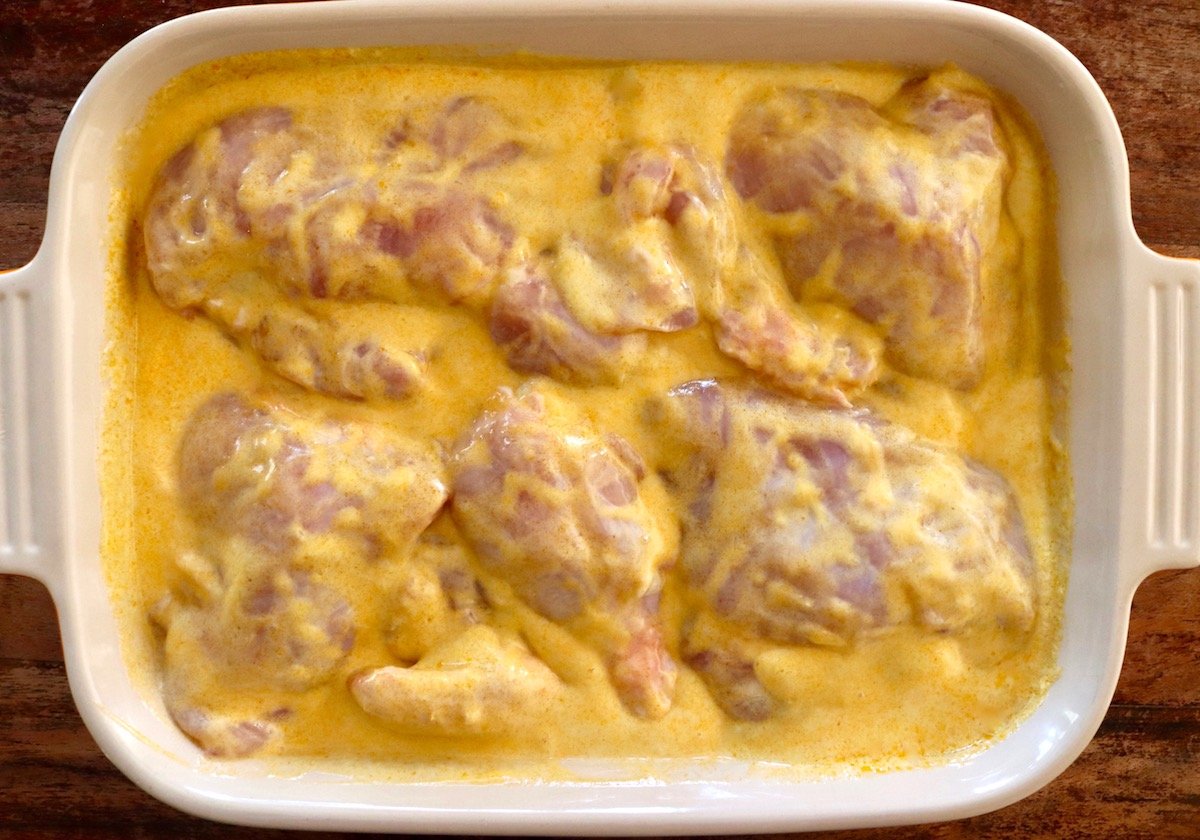 Baking dish with raw chicken pieces on the bone in a creamy coconut mango sauce.
