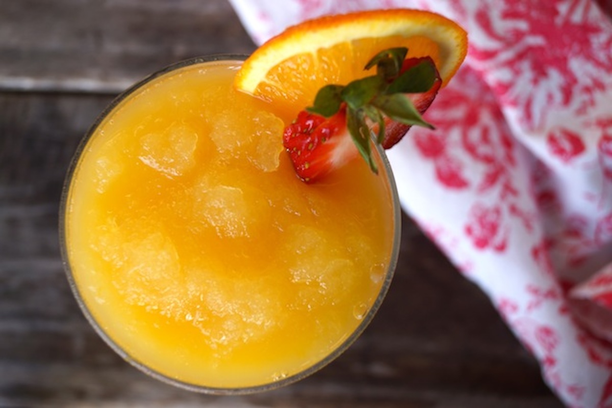 Frozen-Mimosa Top view of a glass filled with frozen mimosa, with an orange slice and strawberry on the rim.