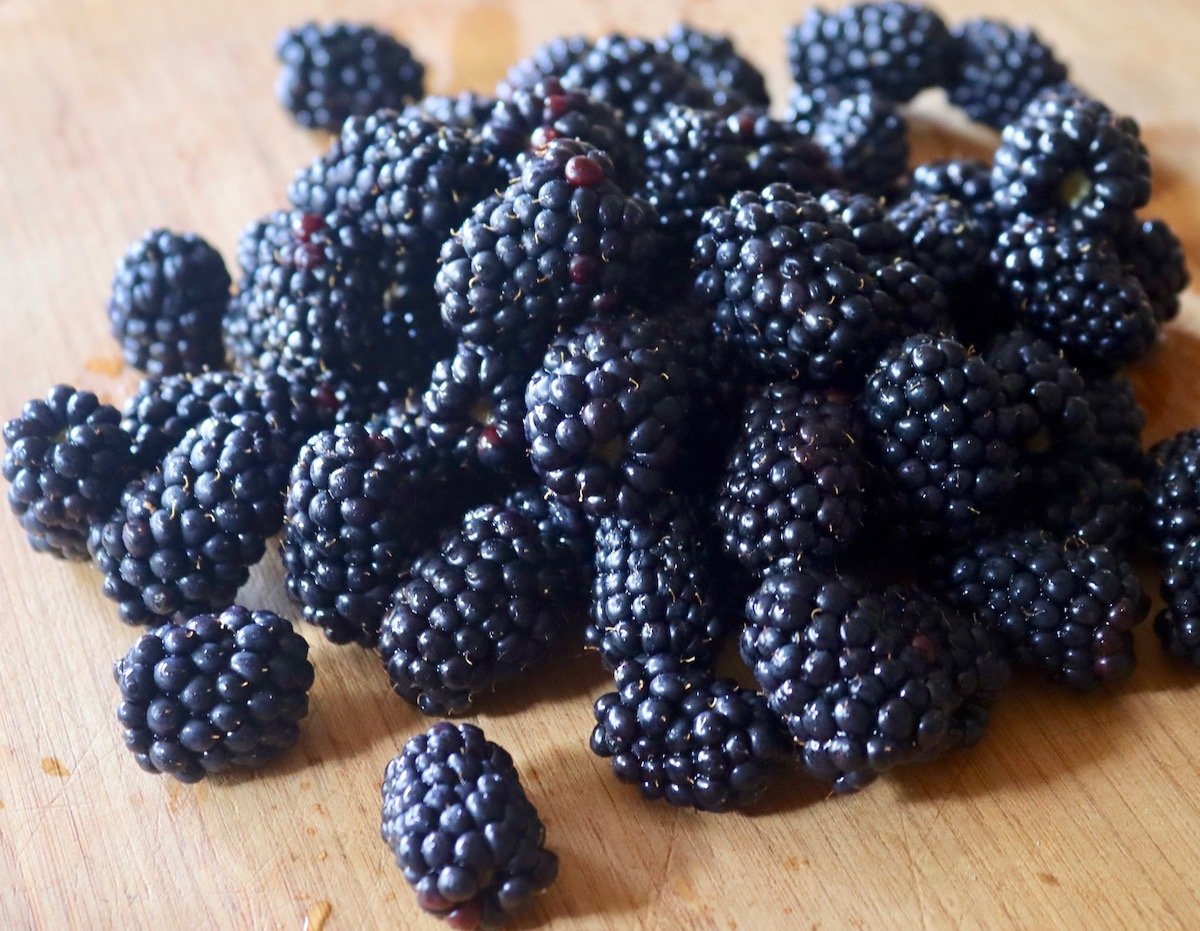 Pile of fresh blackberries on a light wood cutting board.