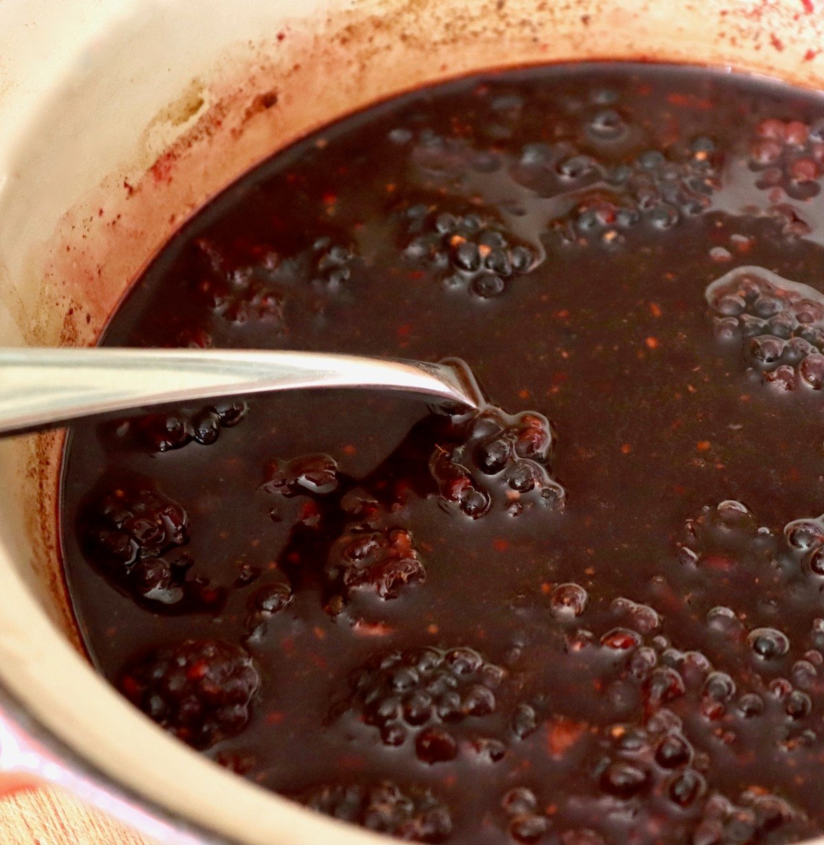 Cooked blackberries and balsamic vinegar, in a small pot with a spoon.