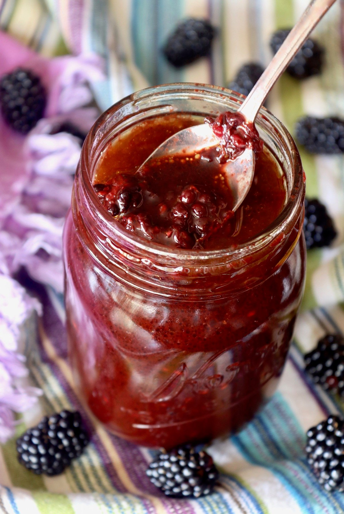 Mason jar full with blackberry vinaigrette with a spoon holding some of it up at the top.