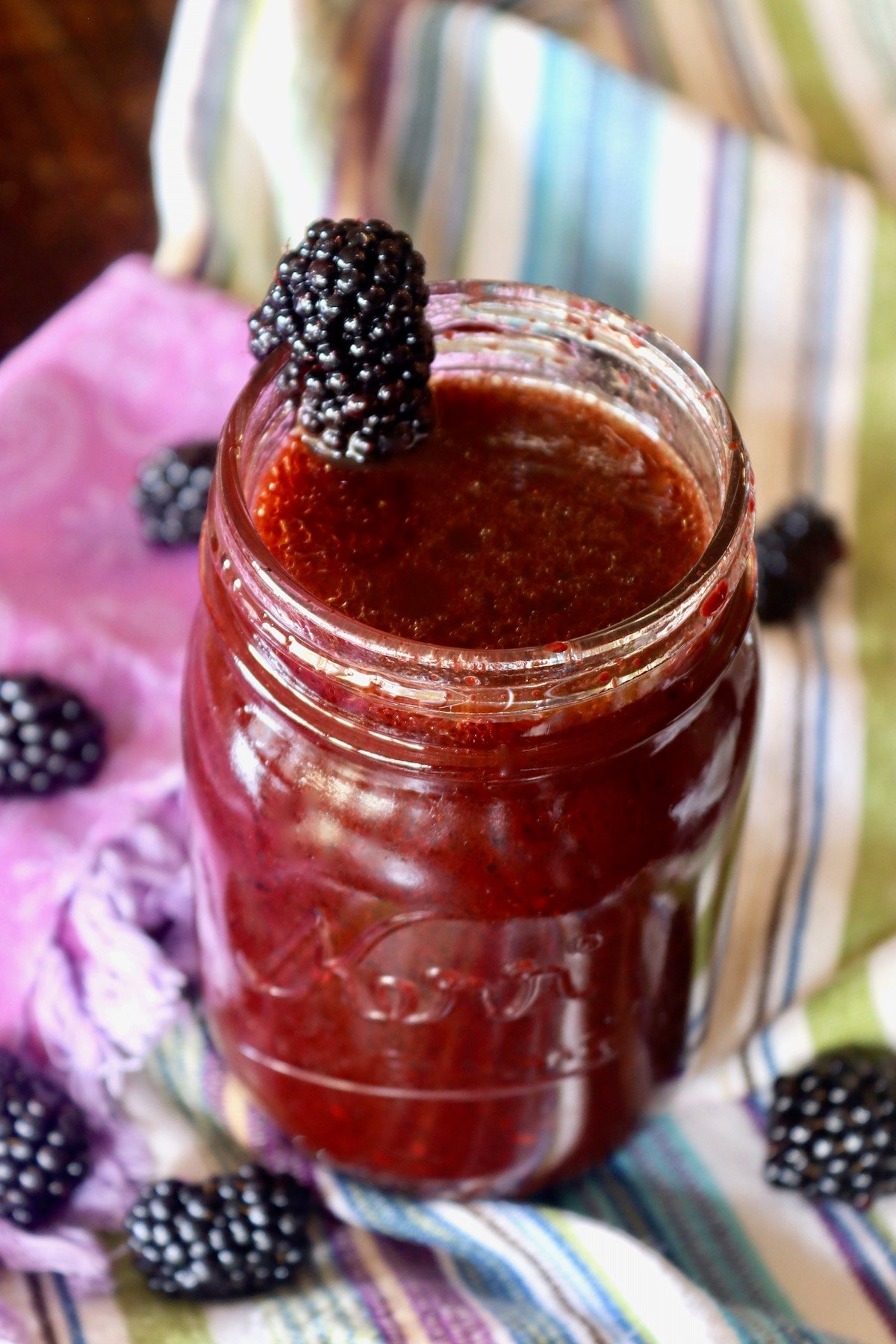 Large Mason jar with blackberry vinaigrette and a whole blackberry on the top rim.