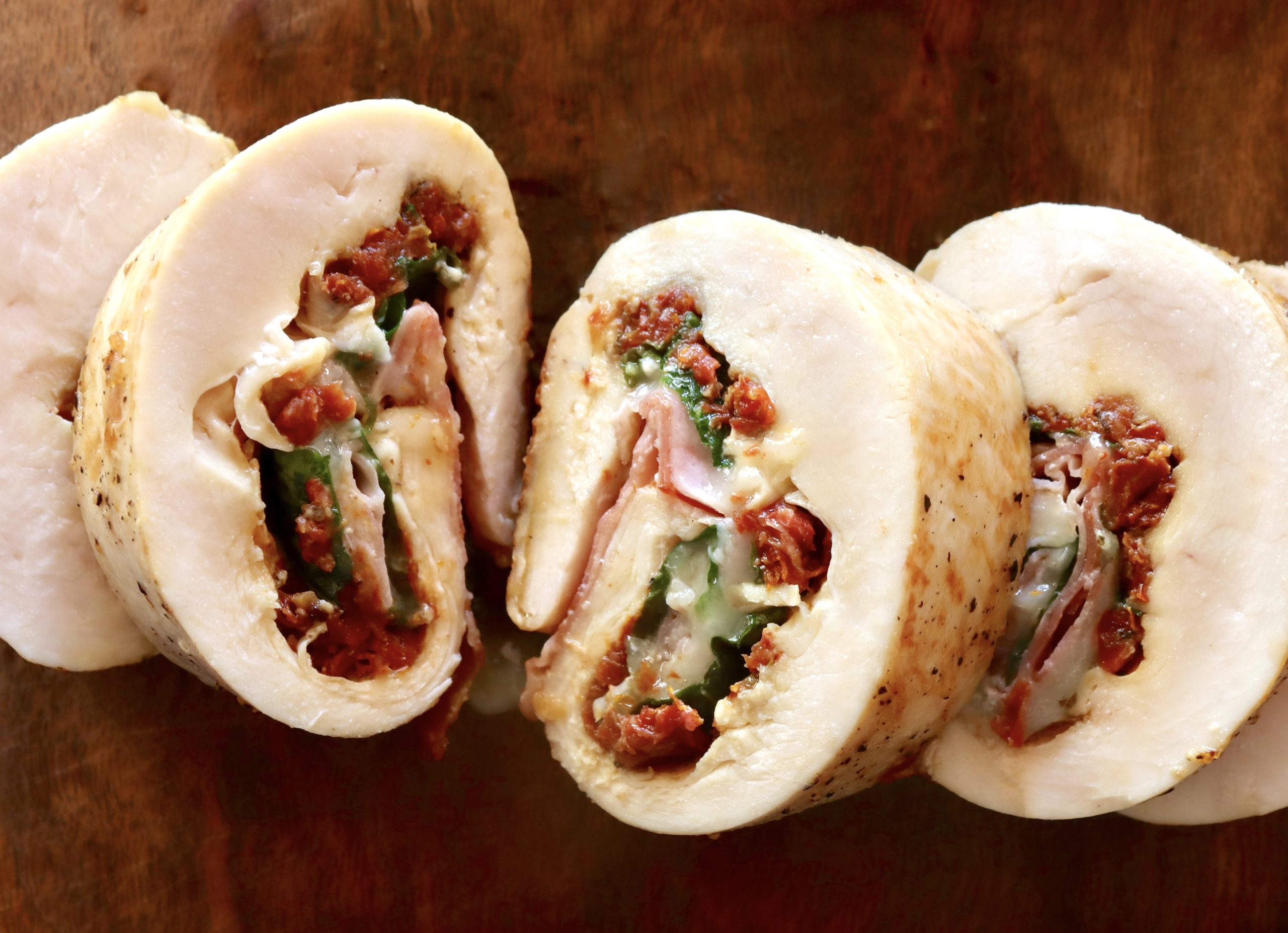 Several slices of a chicken roulade with tomato, basil, cheese and prosciutto filling, on a cutting board.