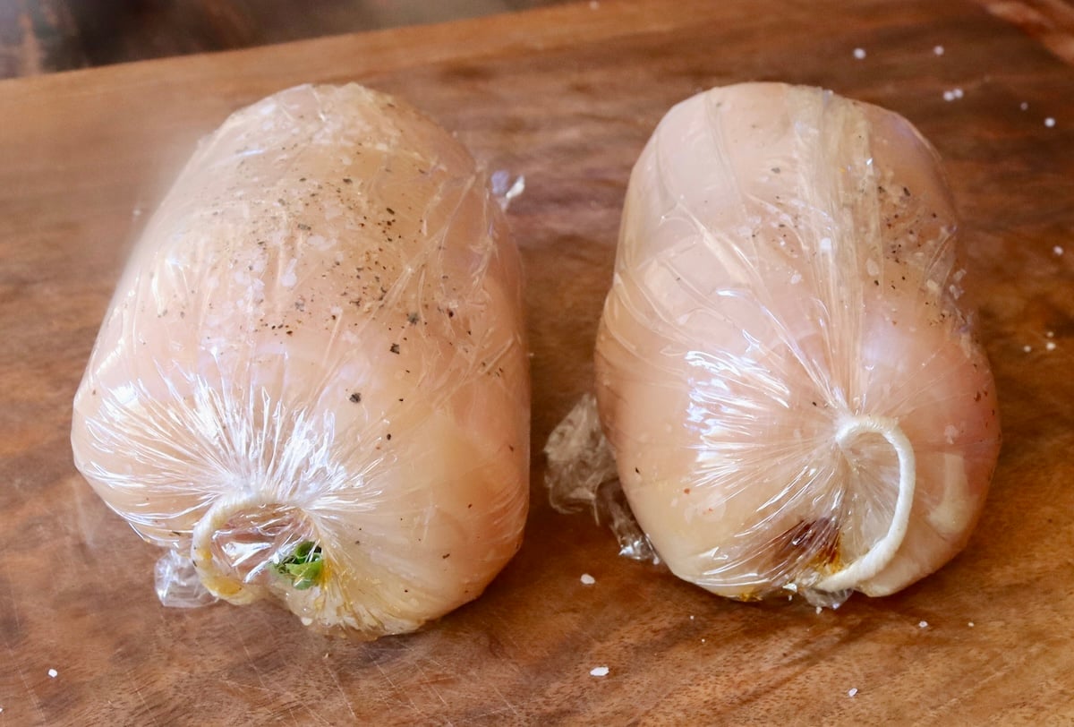 2 rolled raw chicken roulades in plastic wrap.