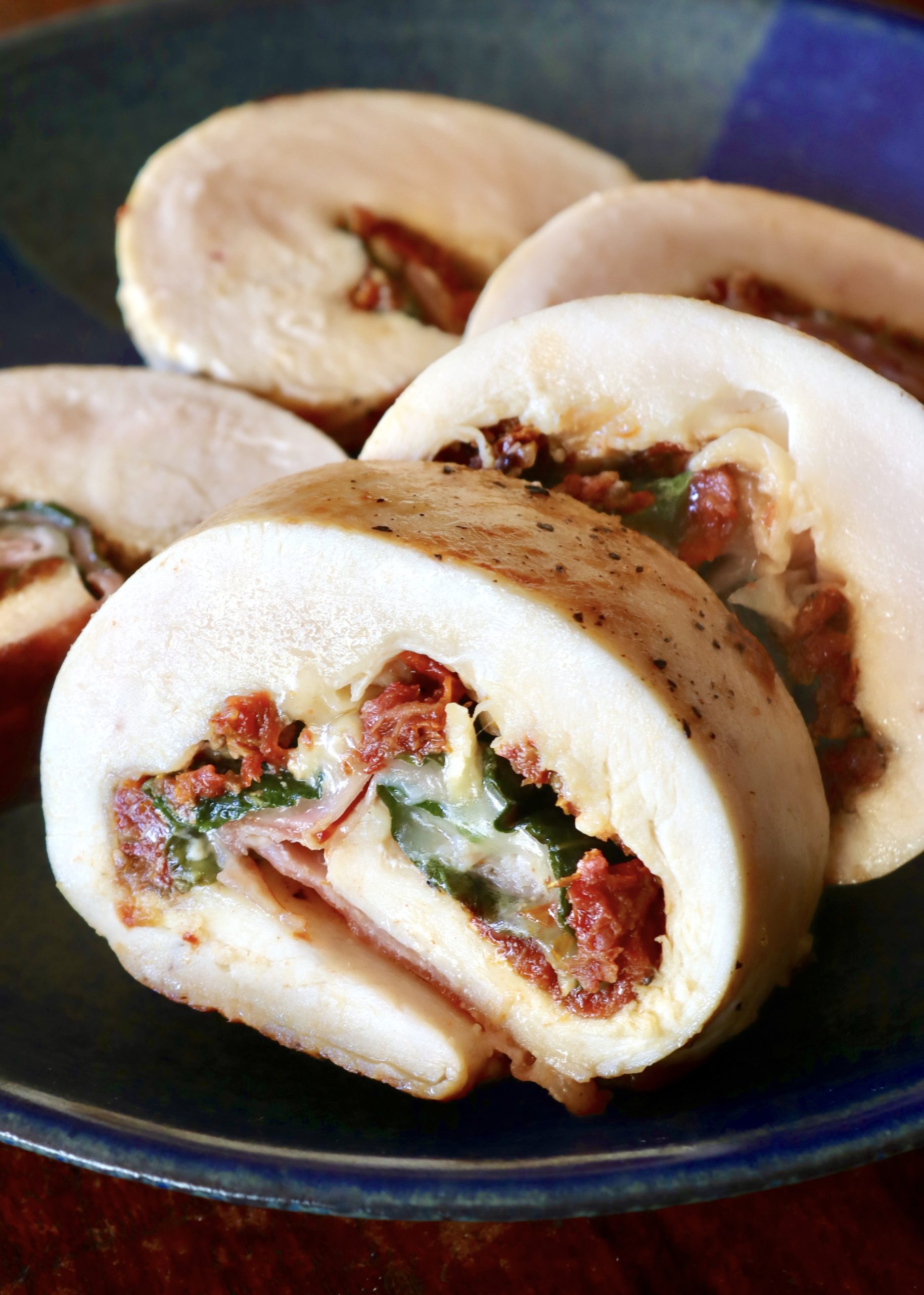 Sliced chicken roulade filled with sun-dried tomato, basil and cheese - on a dark blue plate.