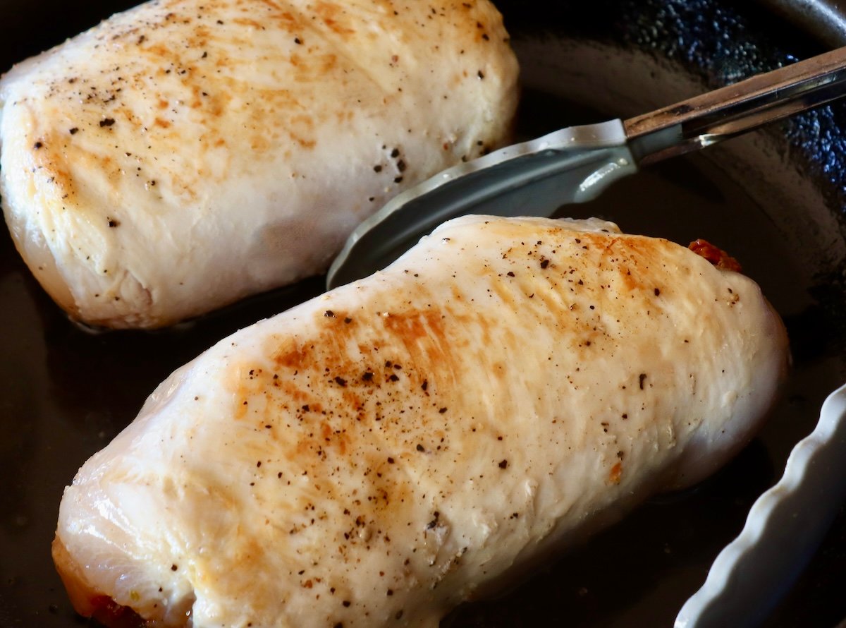 Two browned chicken roulades in a pan with tongs.