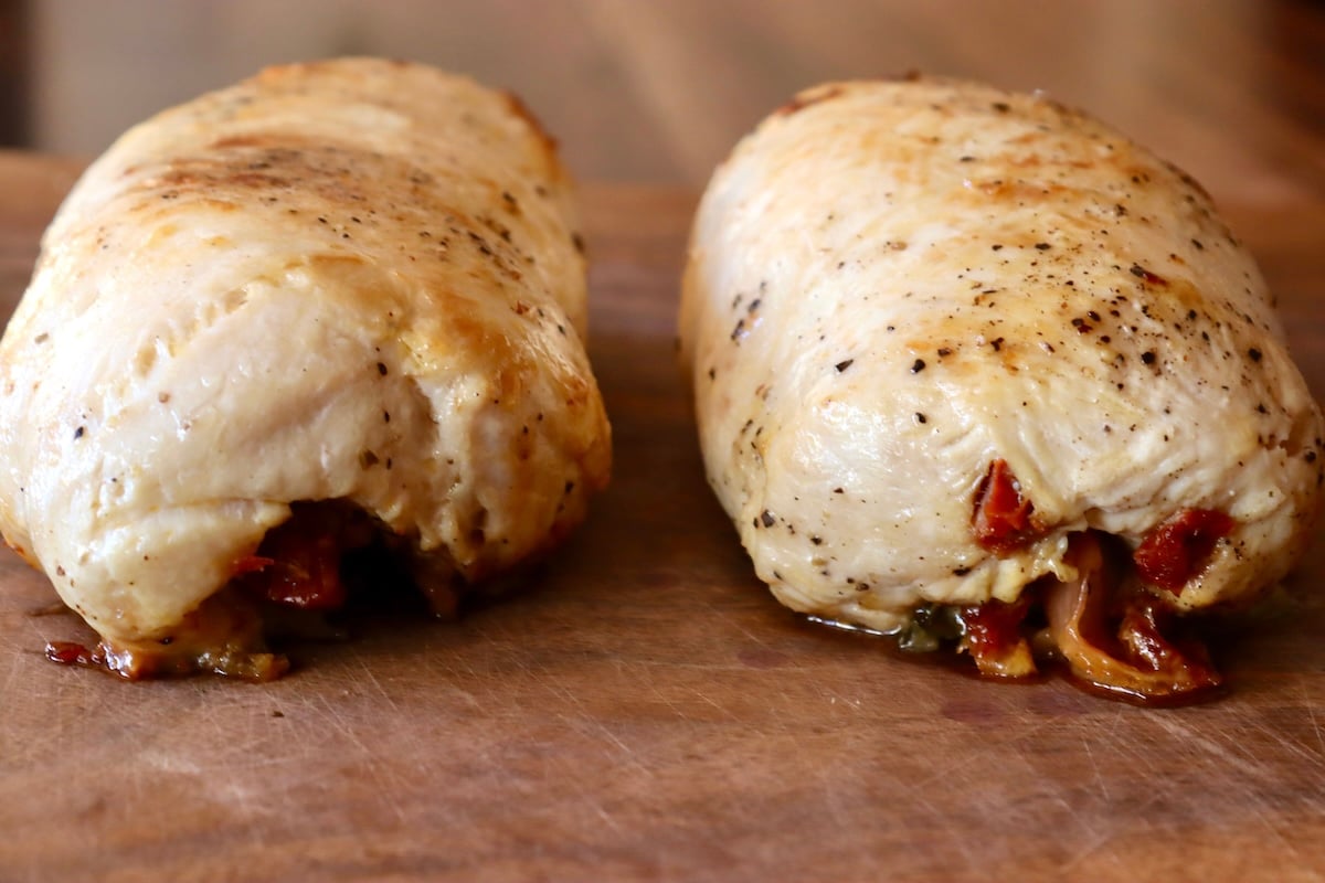 Two cooked chicken roulades on a cutting board.