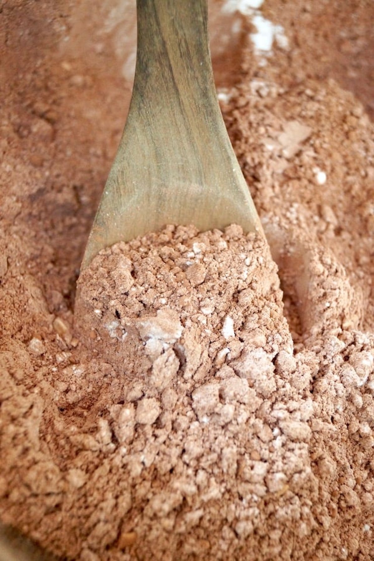 Cocoa powder with wooden spoon in a bowl.