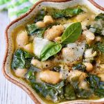 Cream-colored ceramic bowl with crimped edges, filled with Tuscan white bean soup with fresh basil on top.