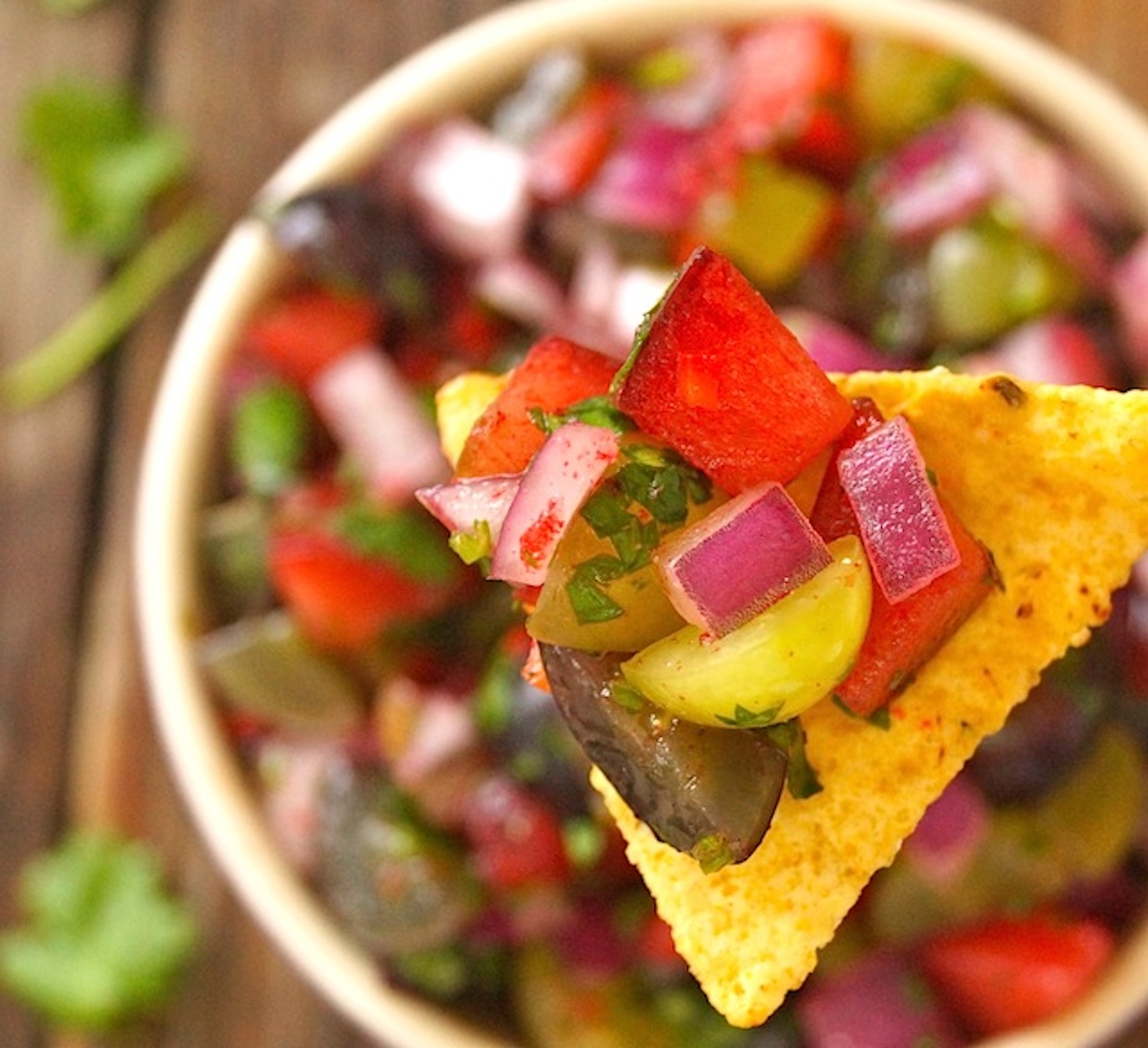Grape-Plum-Summer-Salsa Grape-Plum Summer Salsa on a chip above a bowl filled with it.