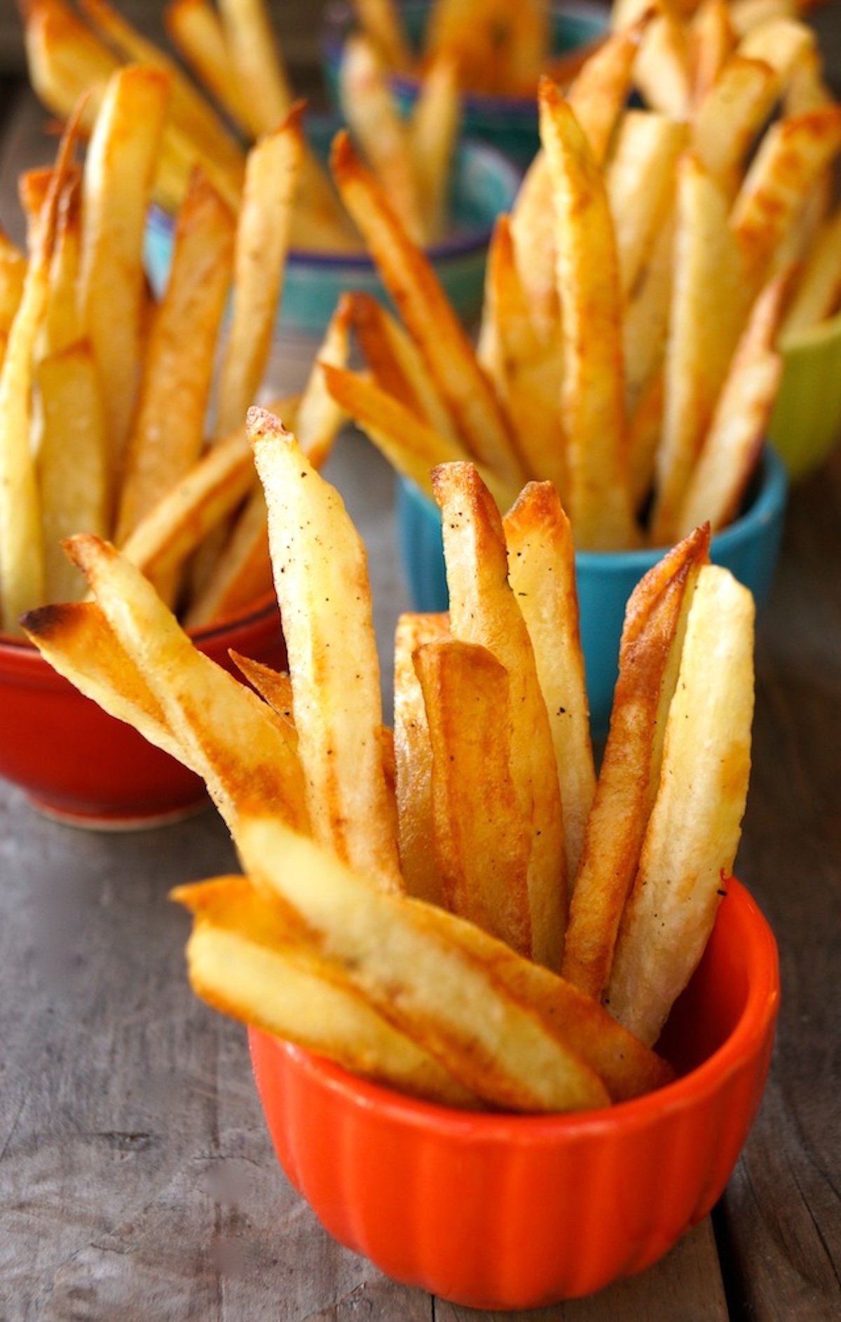 A few colorful bowls holding oven roasted French fries.