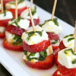 Rectangular white plate with several strawberry caprese on toothpicks.