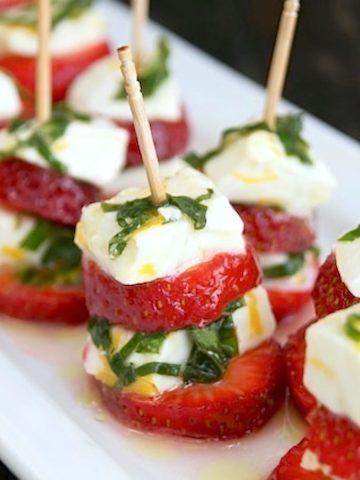 Rectangular white plate with several strawberry caprese on toothpicks.