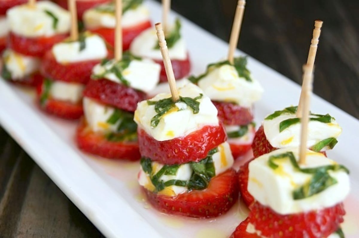 Strawberry-Caprese-with-Lemon-and-Basil Rectangular white plate with several strawberry caprese on toothpicks.