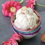 A few scoops of lychee ice cream in a pink-rimmed ceramic bowl with pink Gerbera daisies in the background.