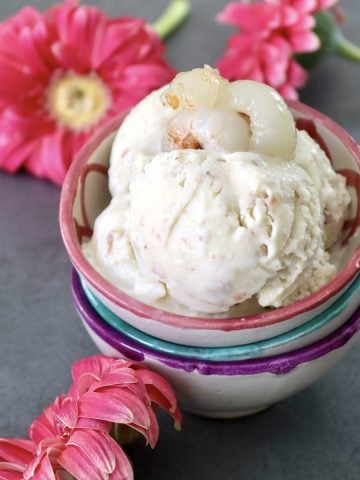 A few scoops of lychee ice cream in a pink-rimmed ceramic bowl with pink Gerbera daisies in the background.