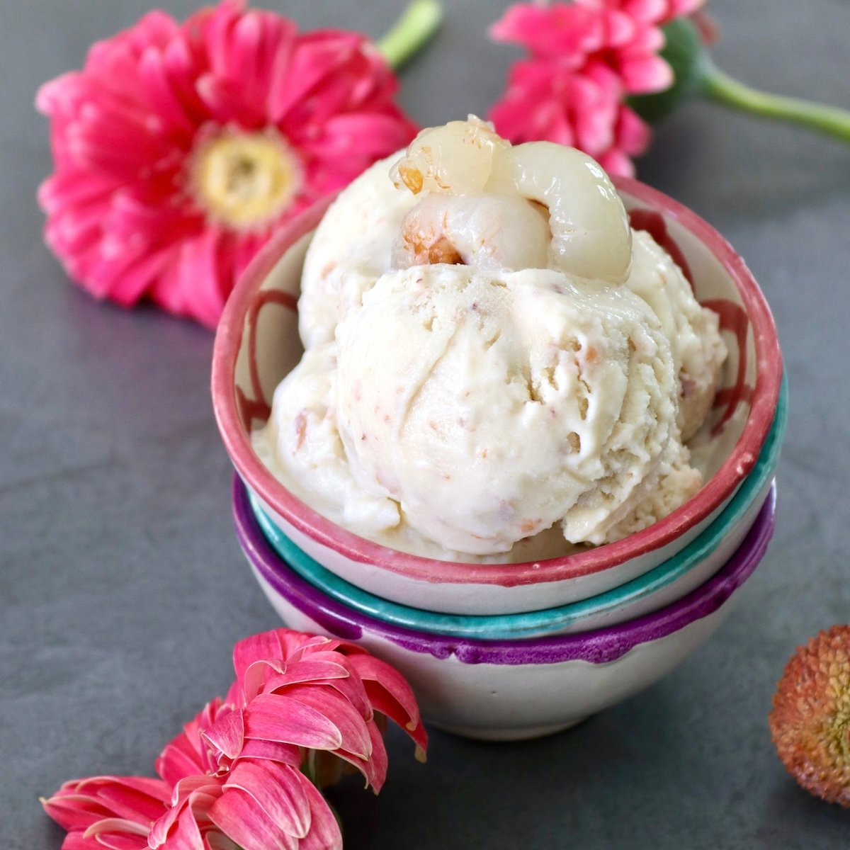 A few scoops of lychee ice cream in a pink-rimmed ceramic bowl with pink Gerbera daisies in the background.
