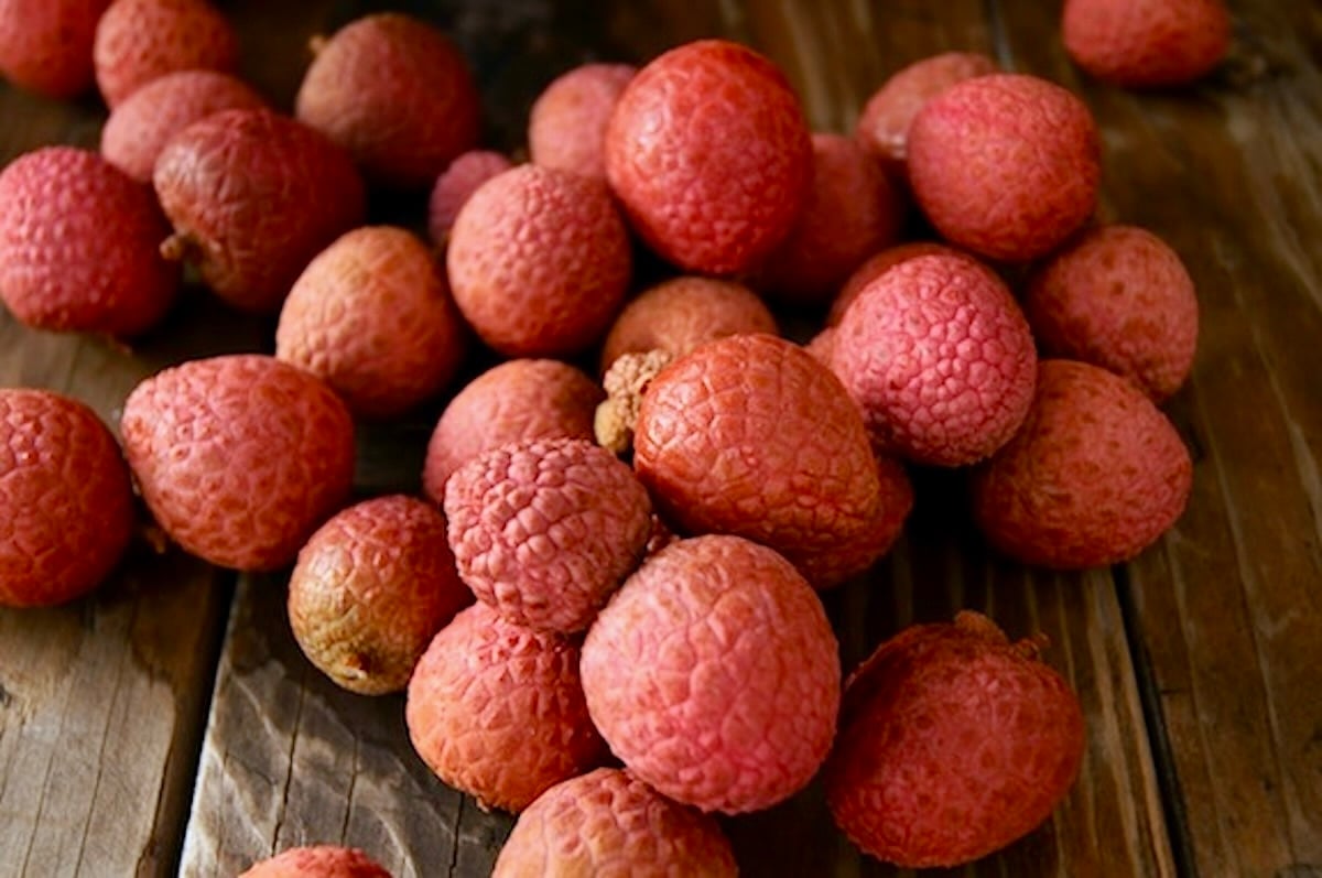 Pile of red-pink Hakip Lychee on a dark wood table.