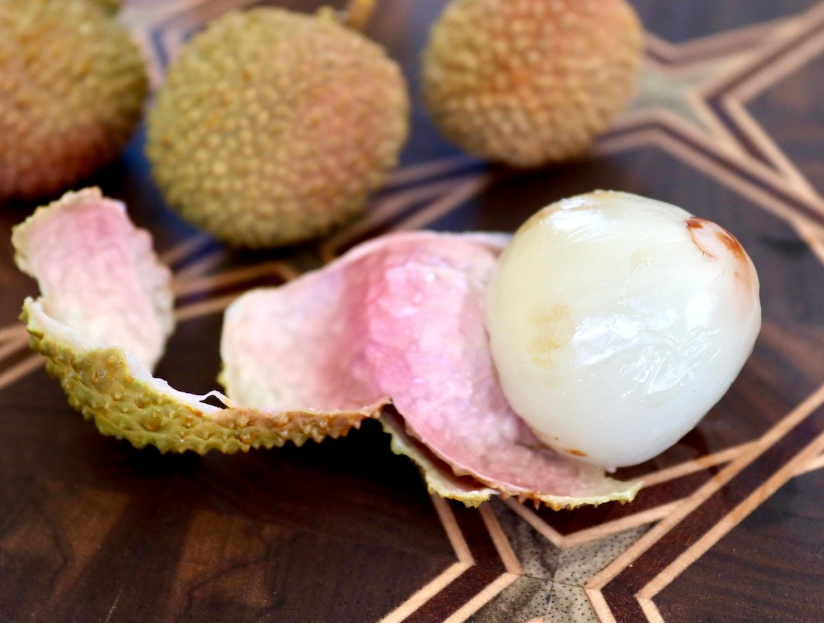 Greenish lychee fruit with the skin peeled off, on a dark wood cutting board.