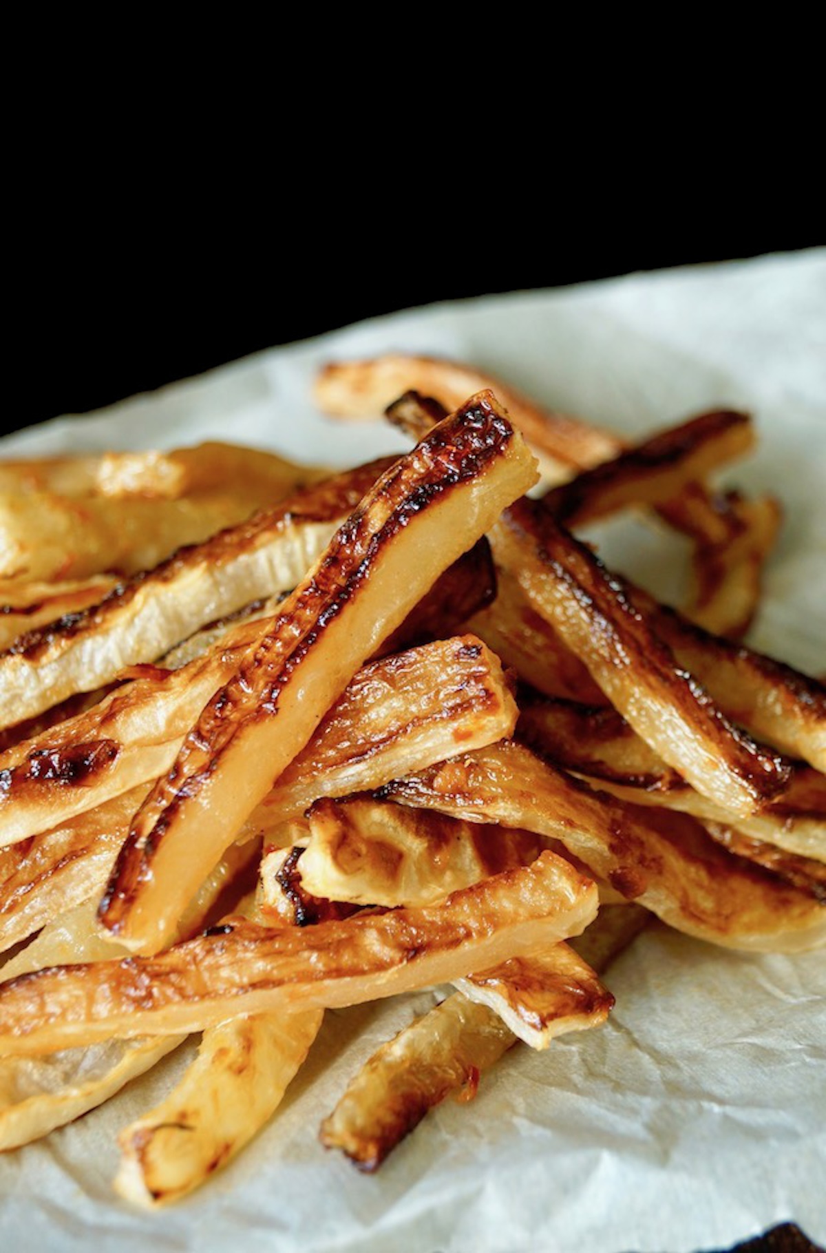 Pile of golden, crispy Daikon Fries on parchment paper.