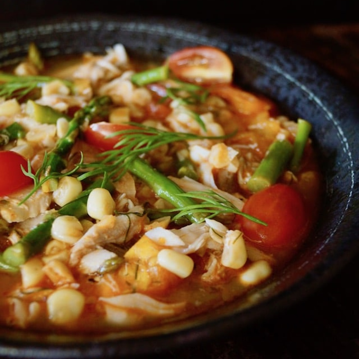 Rich-Slow-Cooked-Flavor—No All-Day-Commitment Light Spring Summer Fish Stew in a black bowl with bright green asparagus and dill on top.