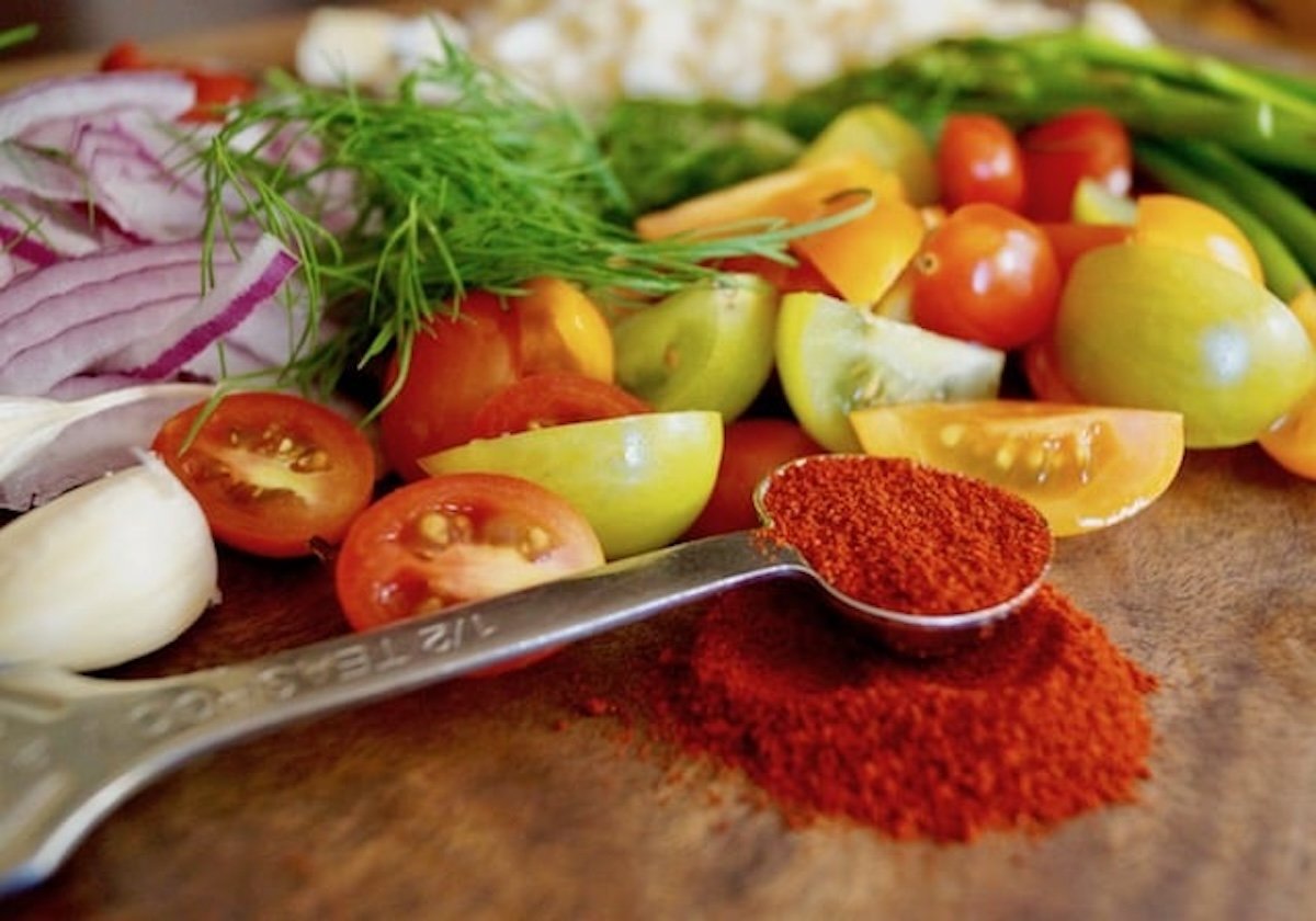 Paprika in measuring spoon with chopped tomatoes and fresh dill on cutting board