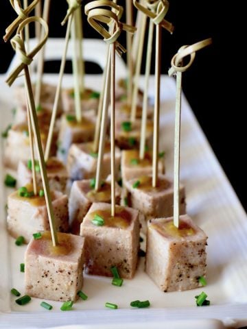 Rectangular white plate with several ahi tuna bites with fresh chives and toothpicks in each one.