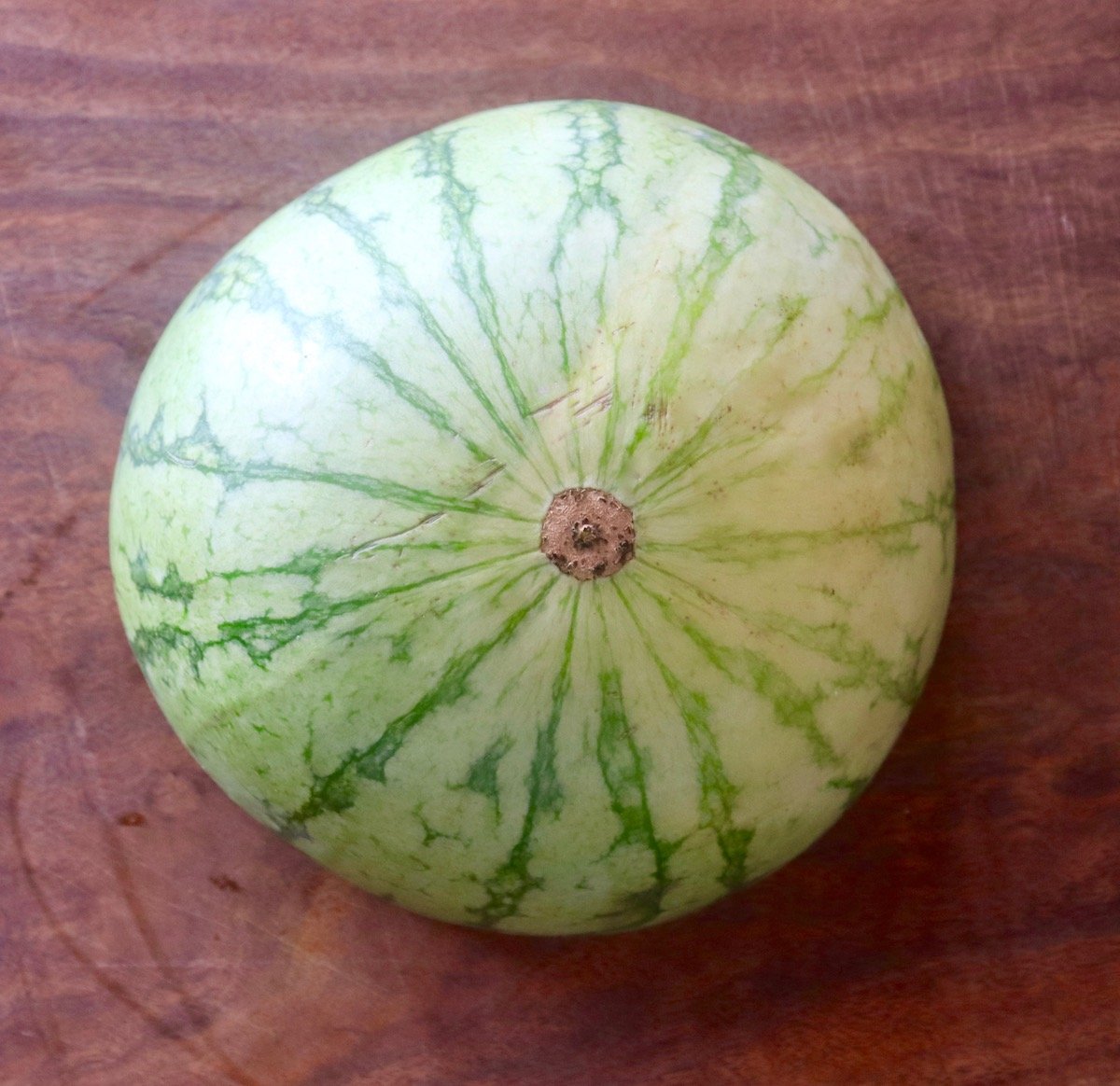 Half of a watermelon, round side up, on dark wood cutting board.