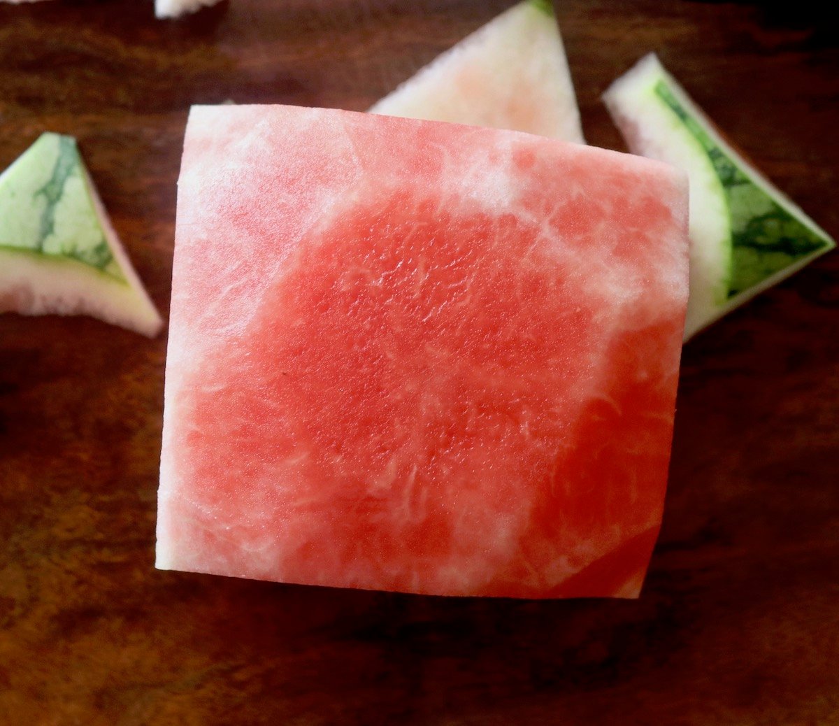 Big, square chunk of watermelon on wooden cutting board.