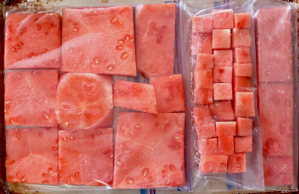 Zip lock bags with watermelon slices and cubes on a sheet pan.