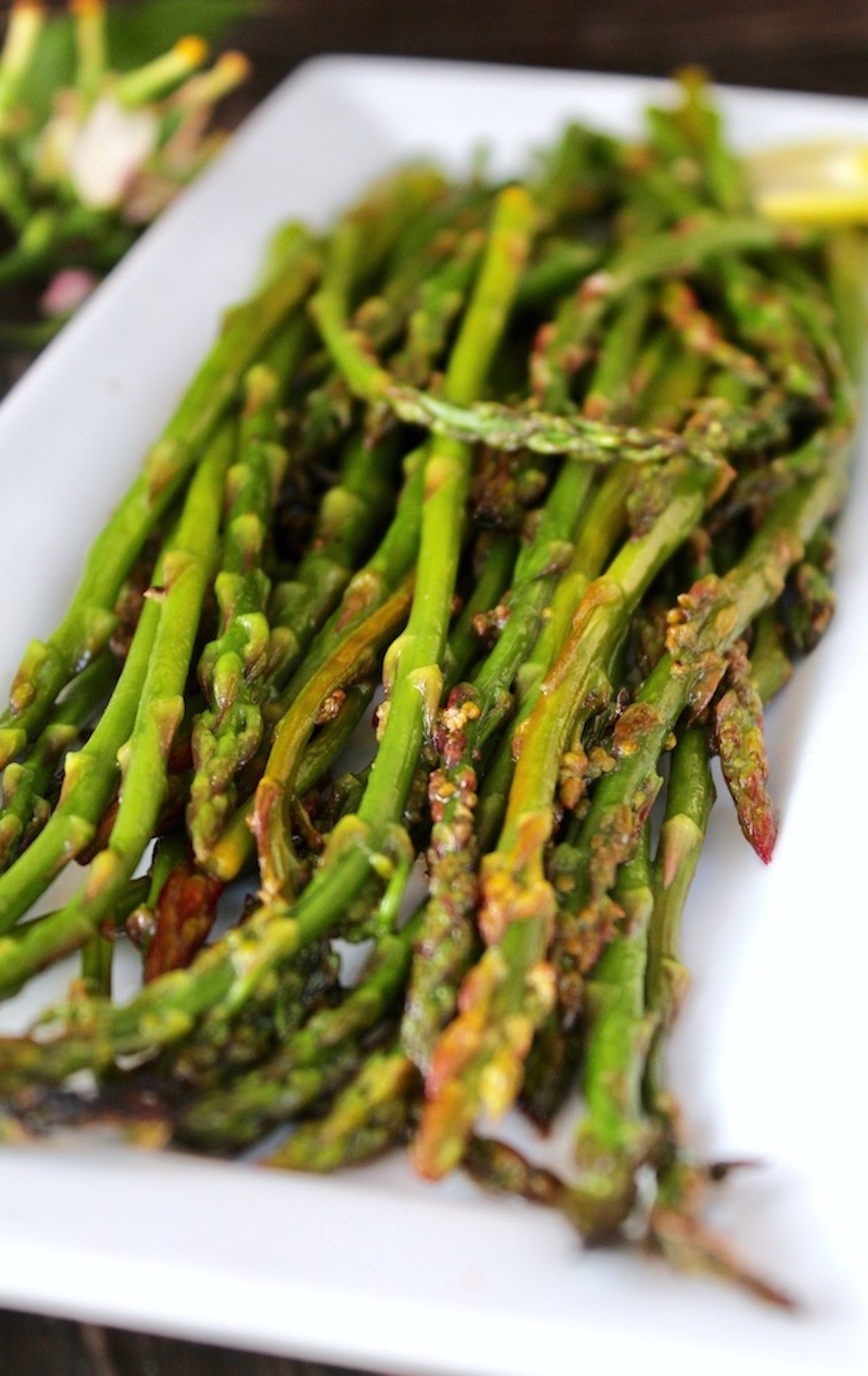 Pile of asparagus on a white plate, that's been grilled with lemon in foil.