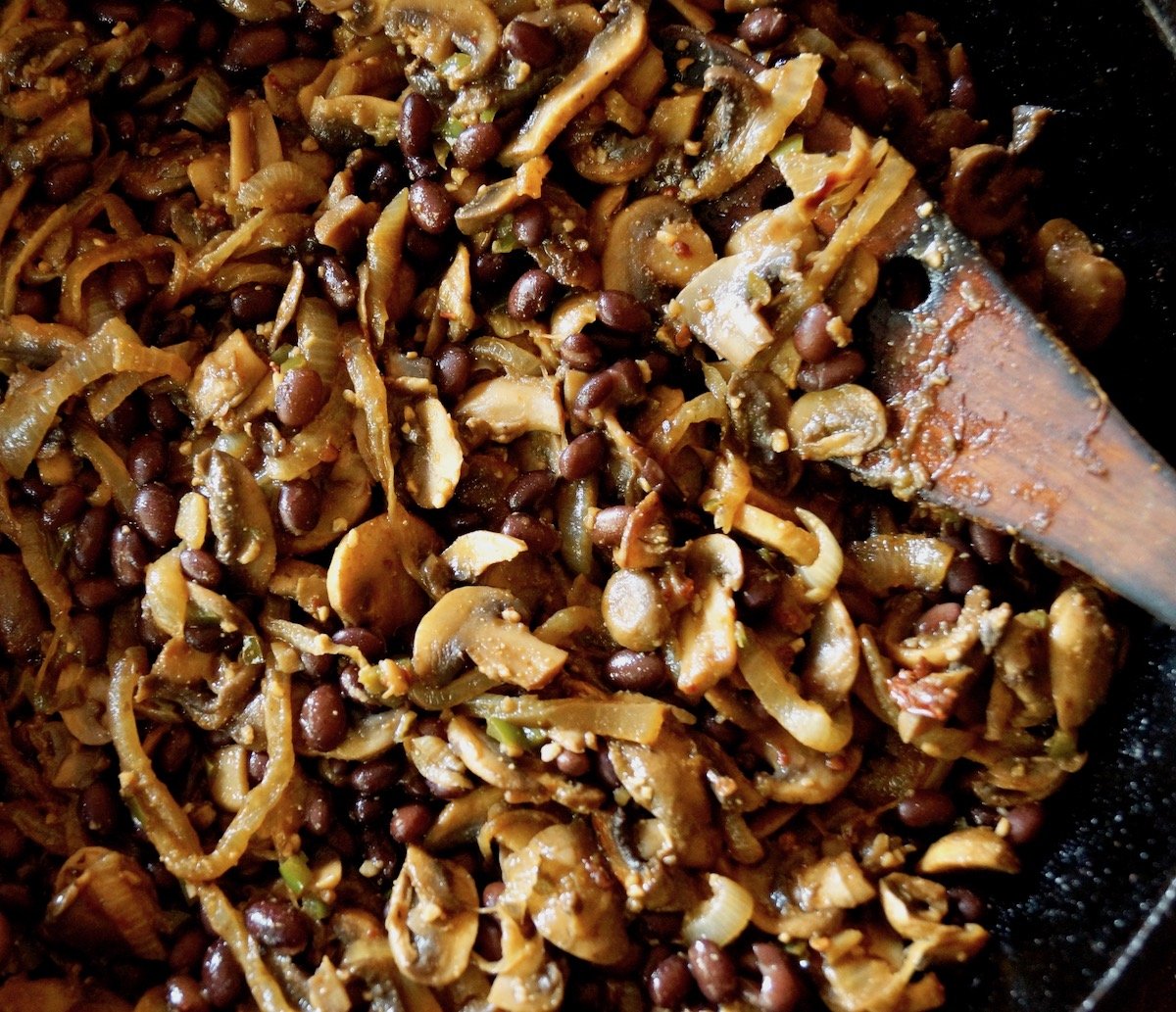 Sauteed onions and mushrooms in saute pan with wooden spatula.