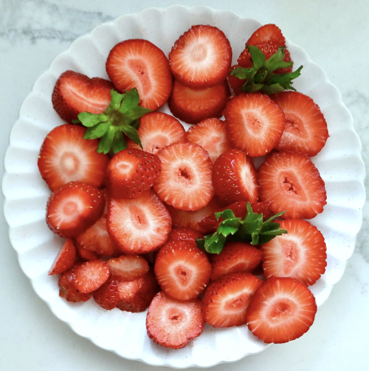 A couple dozen slices of large strawberries on a white crimped-edge plate.
