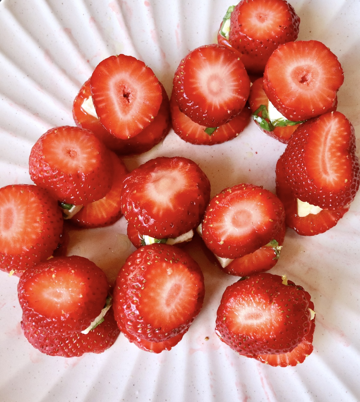 12 tiny stacks of strawberry caprese on a white crimp-edged plate.