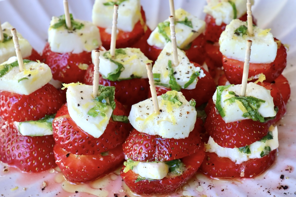 White plate filled with tiny kebabs of strawberry cparese with toothpicks.