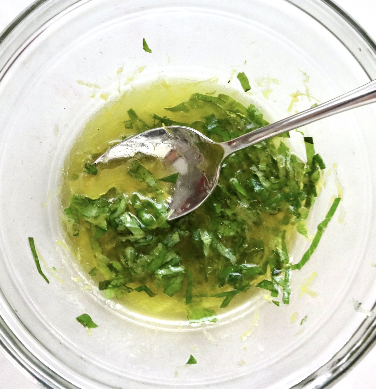 Basil and lemon marinade in a glass bowl with a silver spoon.