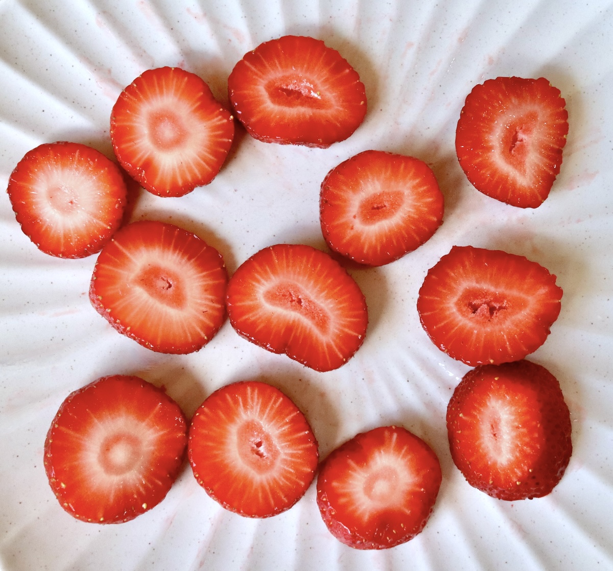 12 slices of fresh strawberries on a white plate.