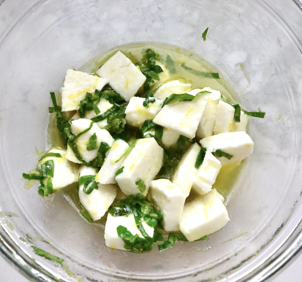 Basil and lemon marinade in a glass bowl with cubed fresh mozzarella.