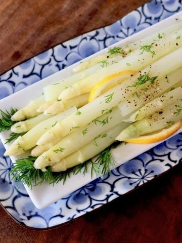 Top view of white asparagus spears on a rectangular place with fresh dill and lemon slices.