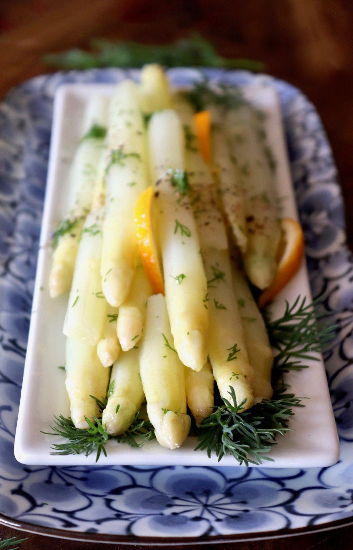 View from spear tips of white asparagus on a rectangular place with fresh dill and lemon slices.