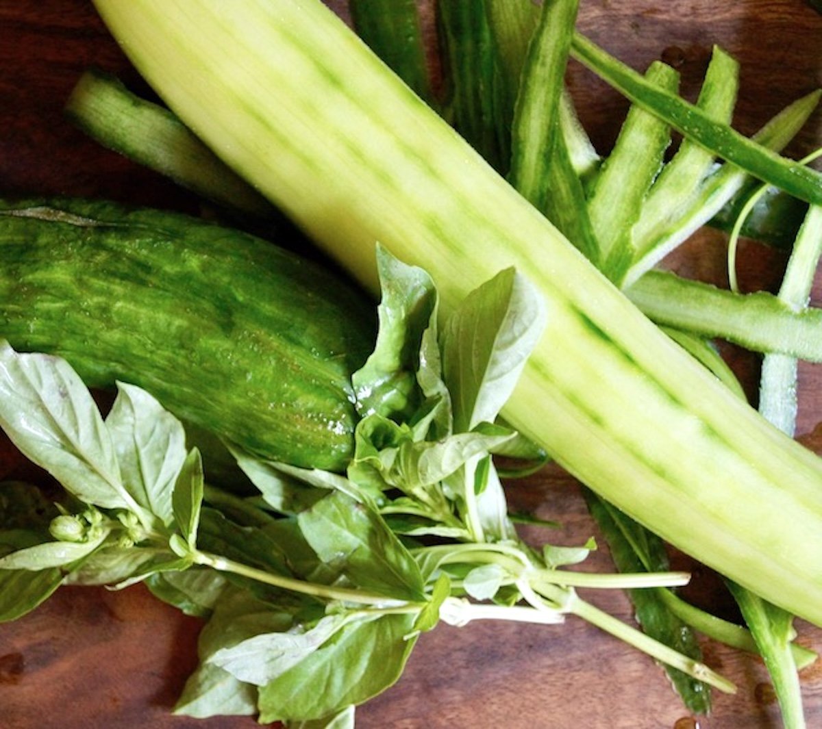 Cucumber and fresh basil on cutting board.